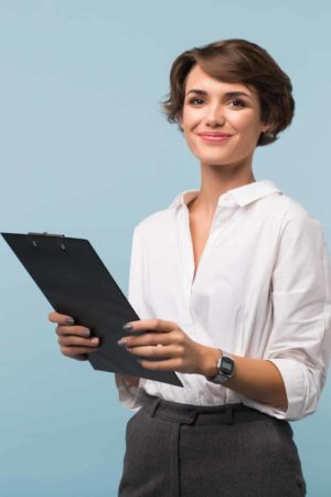 Beautiful business woman with dark short hair in white shirt holding black folder in hands joyfully looking in camera over blue background